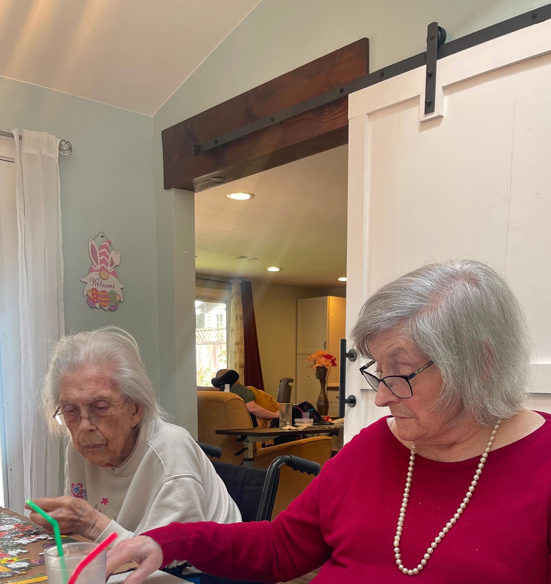 Two residents at Abbey Road Care Homes in Edmonds sitting together at a table, one playing cards and the other working on a jigsaw puzzle